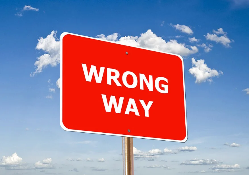 Red road sign reads wrong way with a cloudy sky in the background