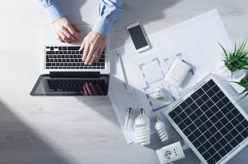 Man working at his desk on a laptop with energy saving CFL lamps, a solar panel and a house project, top view