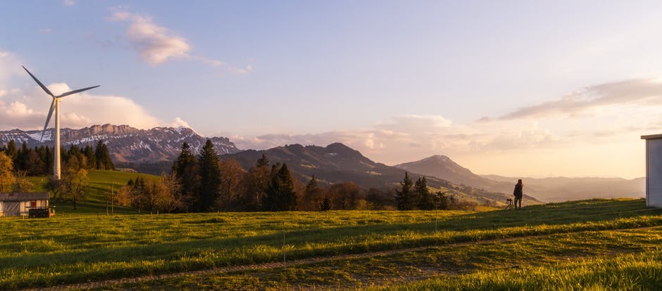 A field at sunrise with a windmill and mountains