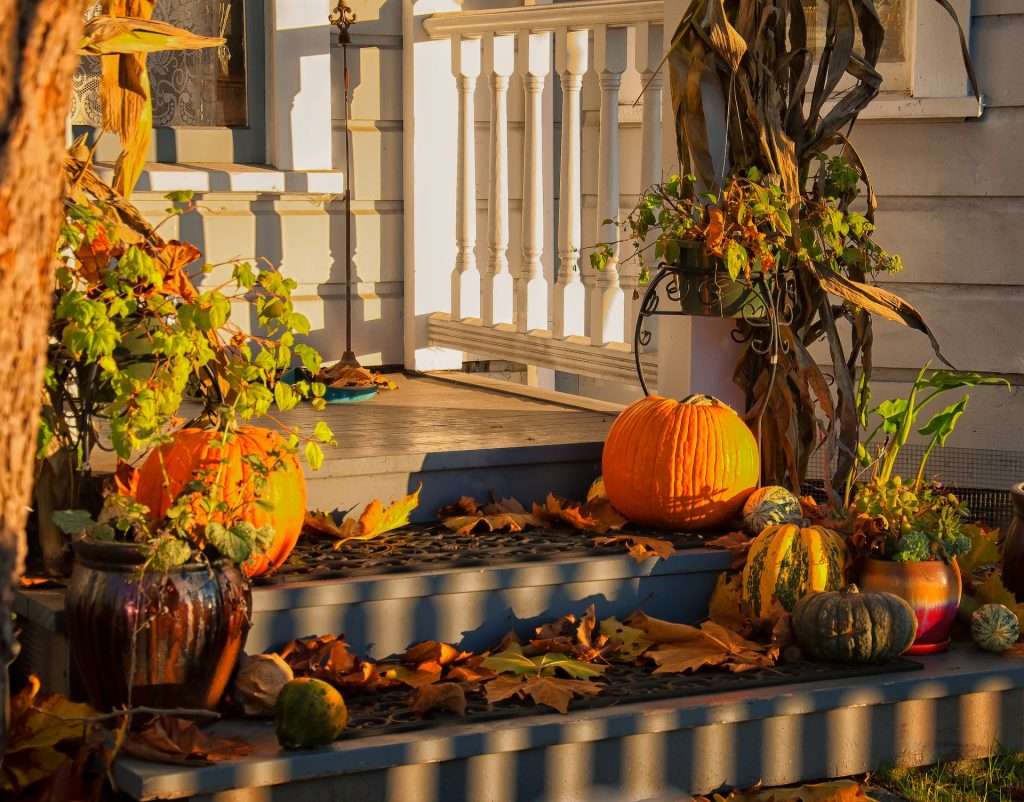 porch festooned with autumn decorations with green materials including pumpkins and cornstalks