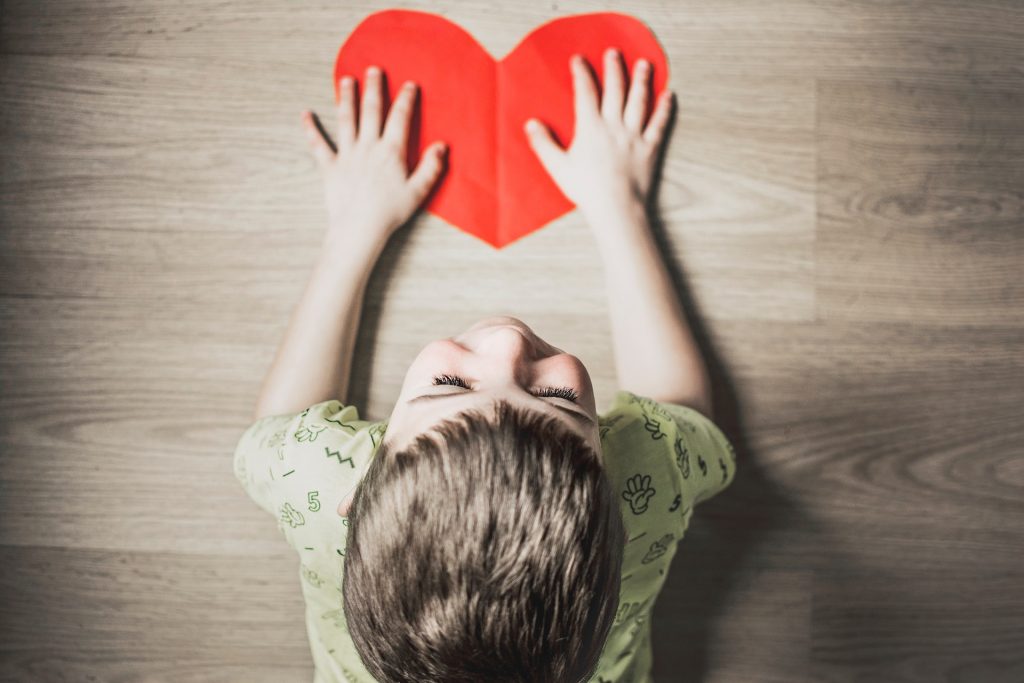 A boy playing on low-VOC flooring with a red paper heart.