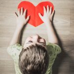 A boy playing on low-VOC flooring with a red paper heart.