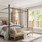 This guest room design uses white and tan colors in the poster bed’s bedding and the rug to create a warmer atmosphere.