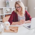 A woman sits in front of a laptop, holding a mug and admiring the white desktop she included in her home office remodel.