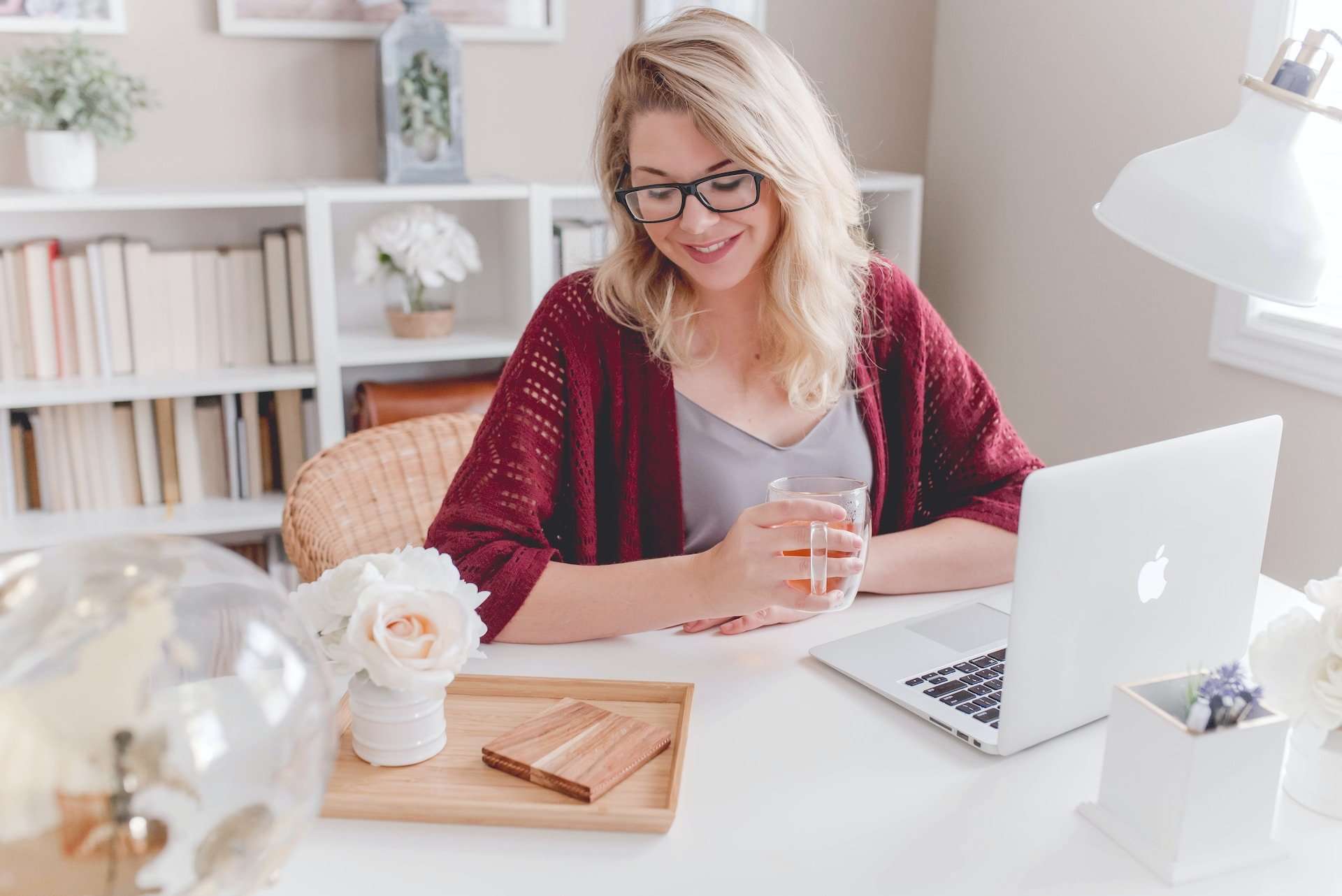 A woman sits in front of a laptop, holding a mug and admiring the white desktop she included in her home office remodel.