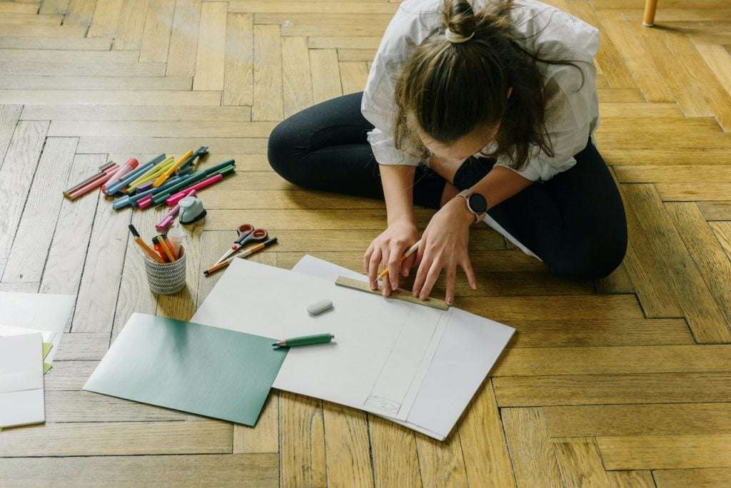 A woman sits on her non-toxic flooring to work with pencils and paper.