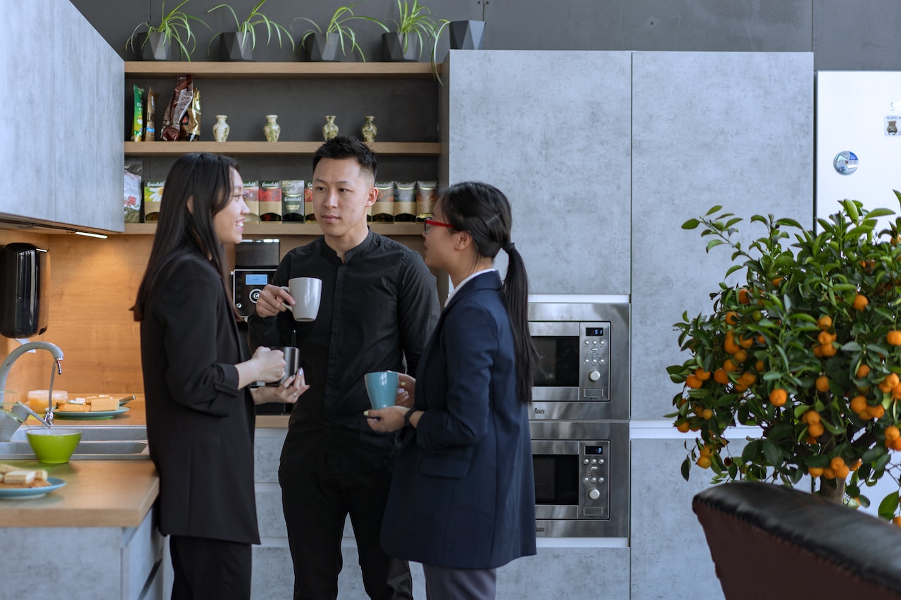 Three employees using personal drinking mugs in the kitchen for a more sustainable office.