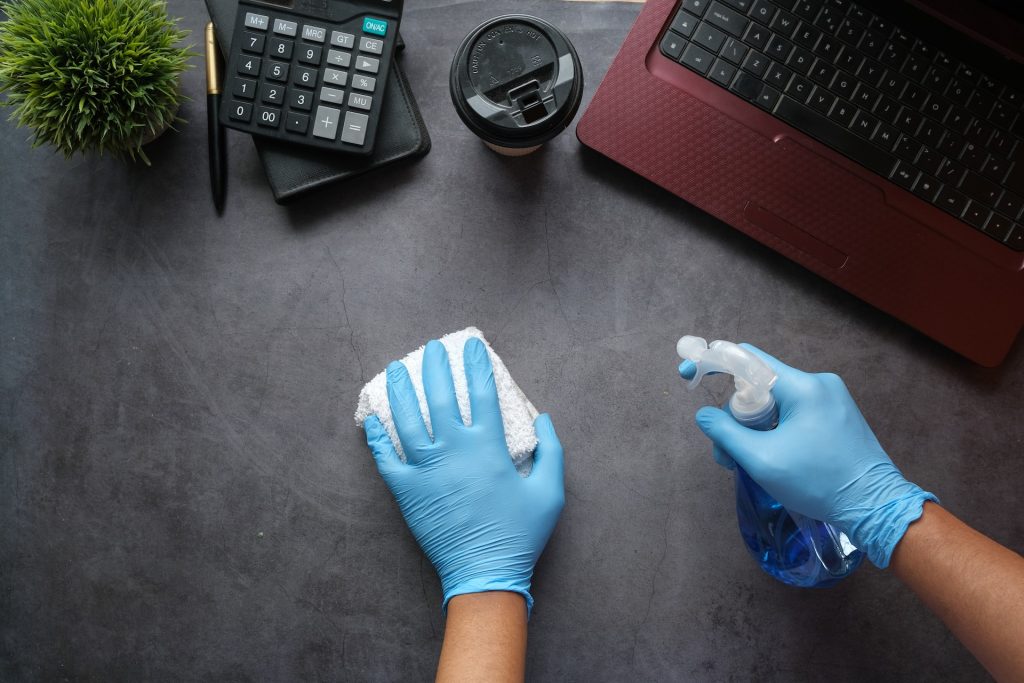 An employee uses eco-friendly cleaners to clean their desk and support sustainability in the workplace.