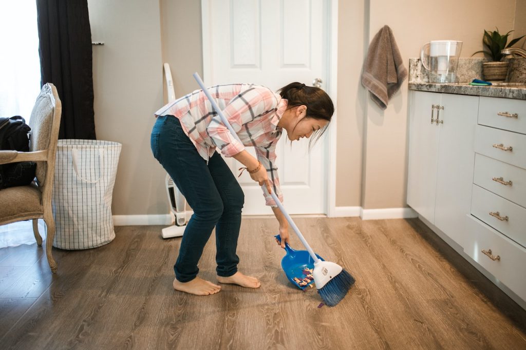 A woman sweeps a room with hardwood plank flooring as she meets her sustainable New Year’s resolutions.