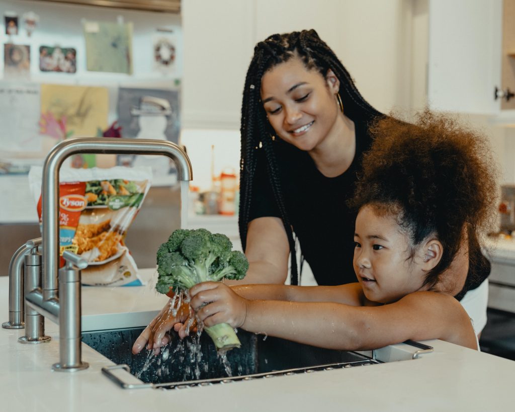 A mother and daughter wash broccoli under a low-flow kitchen faucet that helps them meet their sustainable goals.